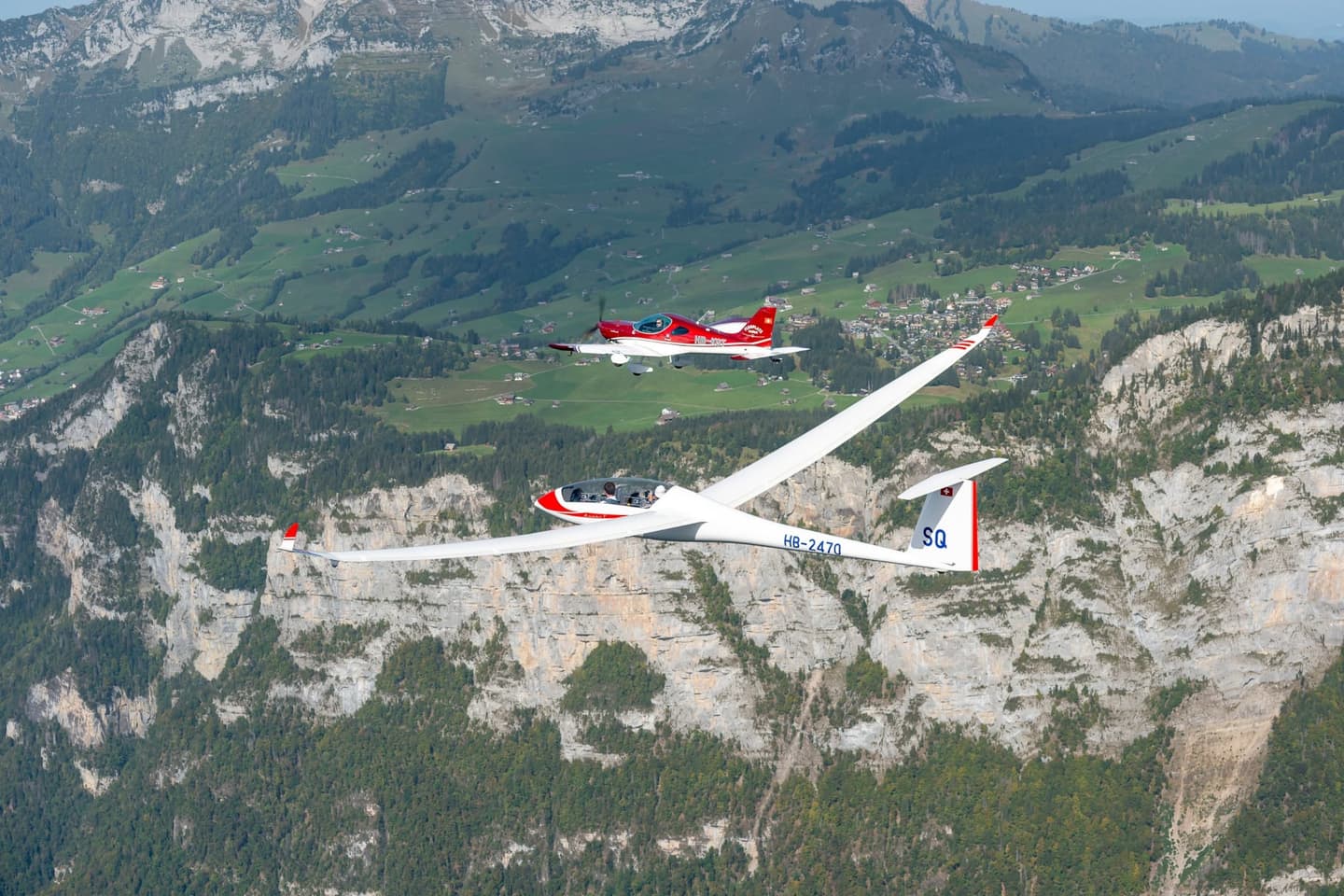 A red Bristell aircraft towing a glider over the Swiss Alps