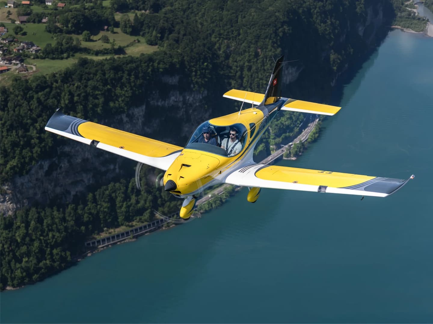 Two pilots in a yellow Swiss-registered Bristell B23 flying over a lake