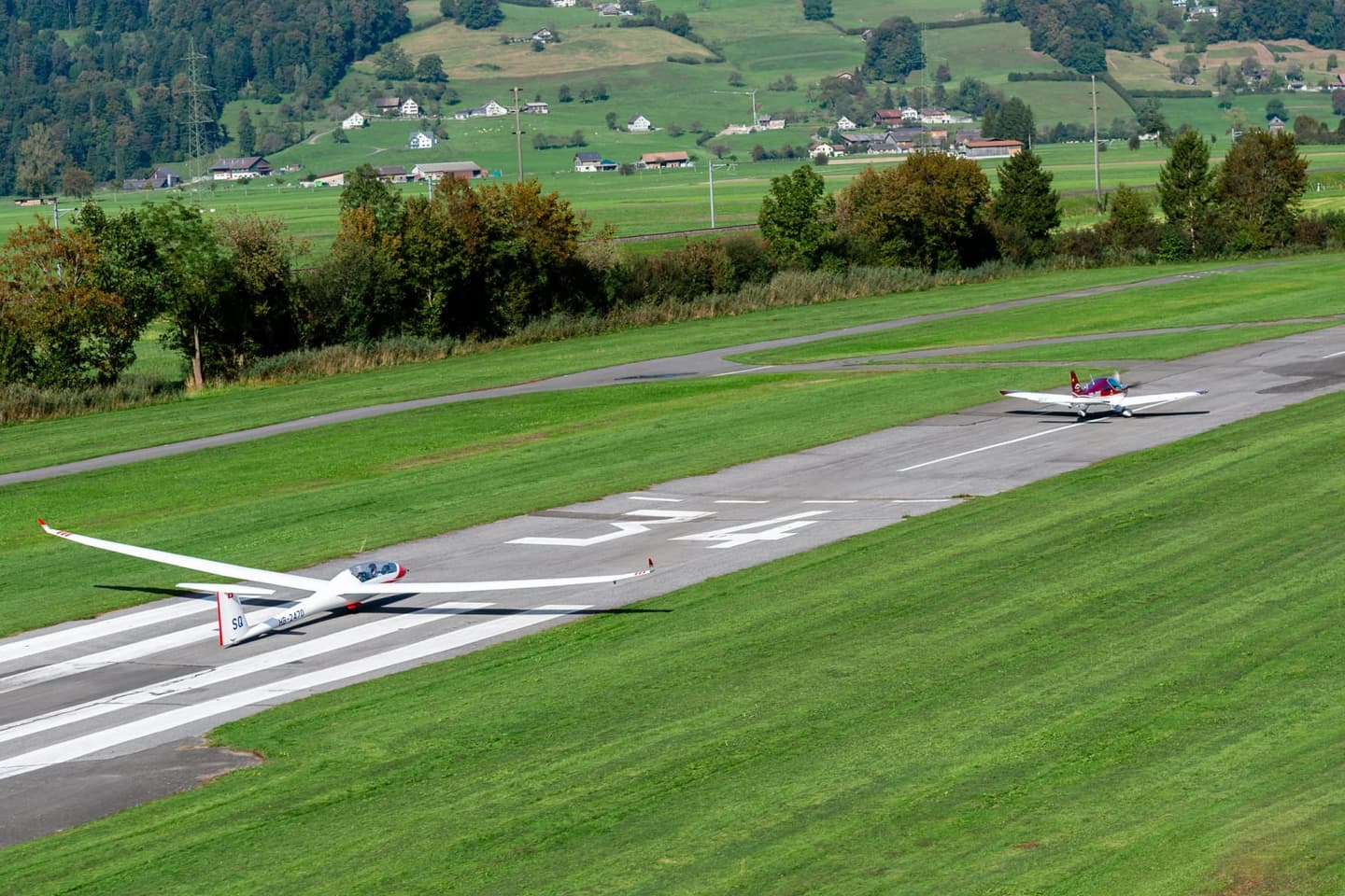 A glider and a red Bristell aircraft together on the runway after a tow