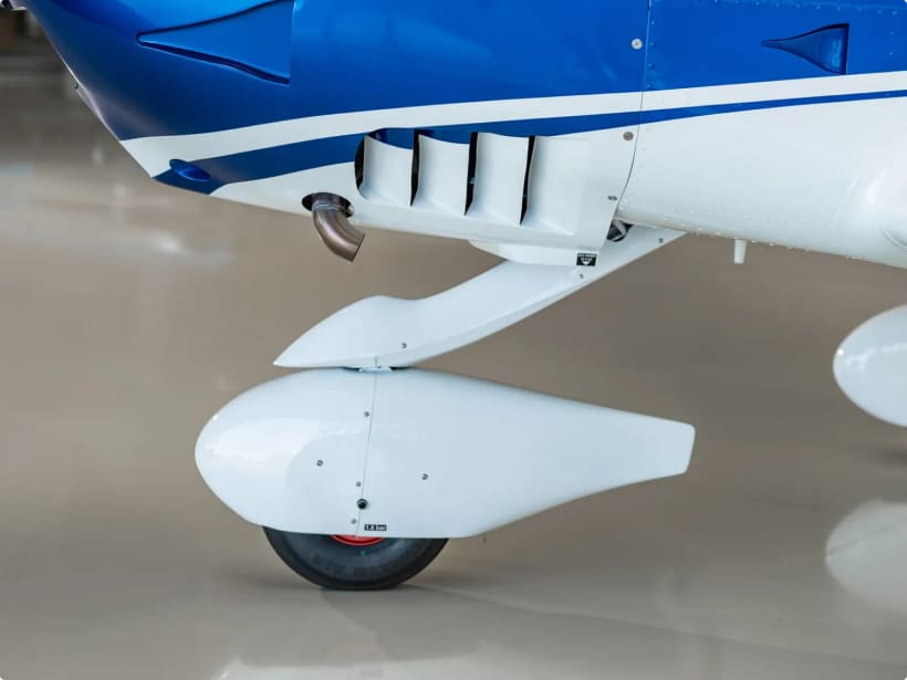 Chrome exhaust silencer outlet beneath the blue-and-white cowling of a Bristell, above the nose-wheel fairing.