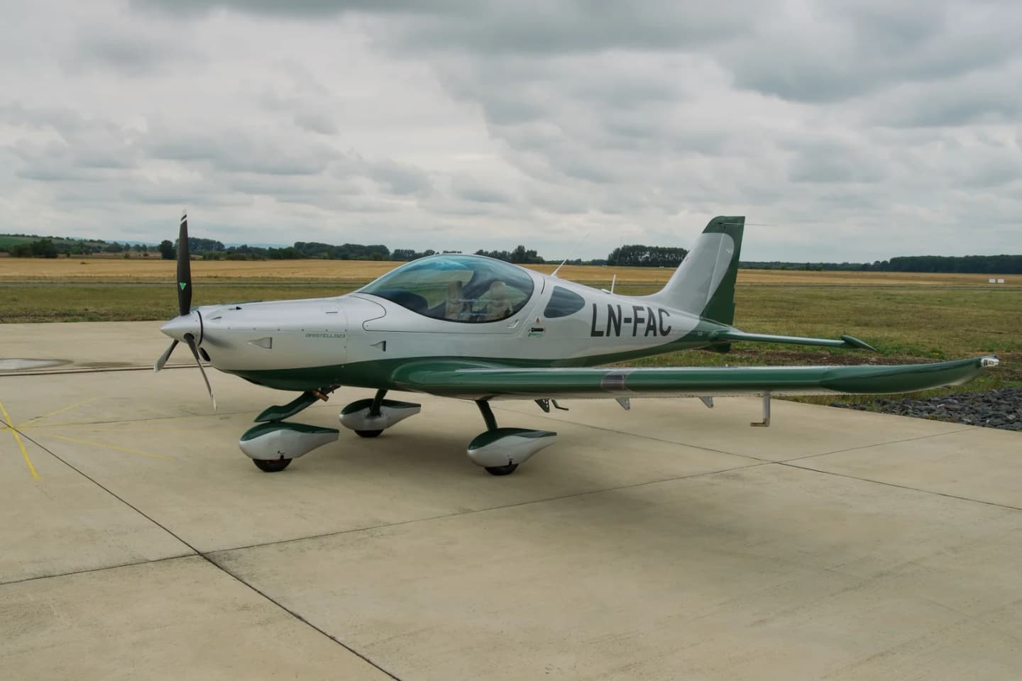 Bristell B23 registered LN-FAC parked on the apron in side view, silver upper fuselage with green wings, wheel spats and tail