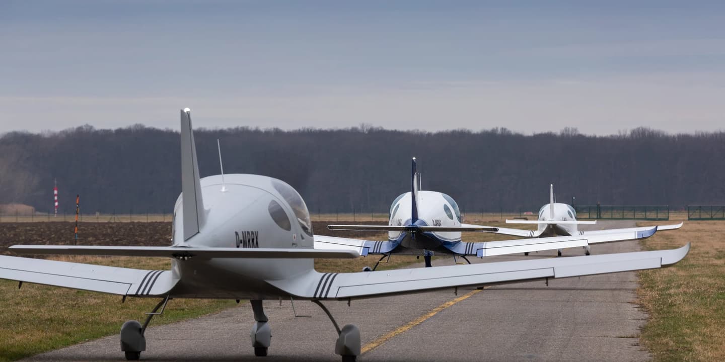 Three Bristell light aircraft lined up on an airfield taxiway, seen from behind